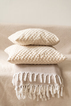 Cozy home decor, textured beige pillows stacked atop patterned throw with white fringe on beige sofa, set against neutral background. Quiet luxury aesthetic, cozy home accessories