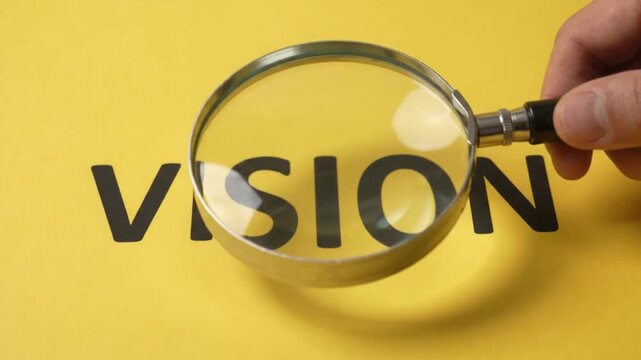 Close-up of magnifying glass focusing on the word Vision on bright yellow background - Conceptual Business and Strategy Image