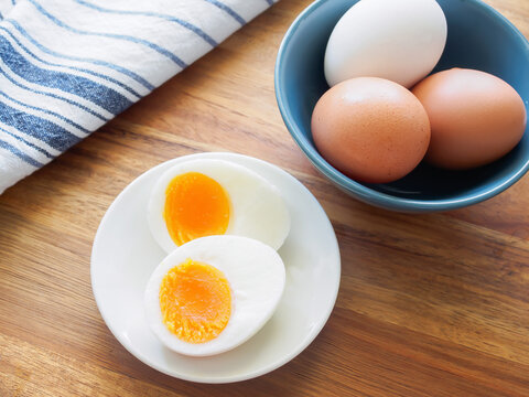 Soft boiled egg cut in half on a white plate and white and brown eggs in a blue bowl on a wooden table