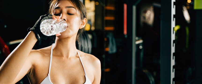 Asian woman guy hydrated by drinking water sports from a bottle in gym after cardio work out, female tired with liquid bottle drink after training at fitness gym, workout healthy lifestyle