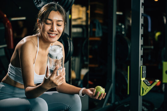 Asian woman holding a green apple and a water bottle in a fitness gym