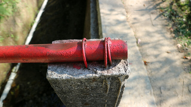 Close up of red painted metal pipe fixed on concrete post outdoors