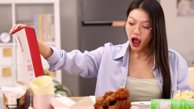 Excited Asian Woman Opening Takeout Pizza Box at Dinner Table