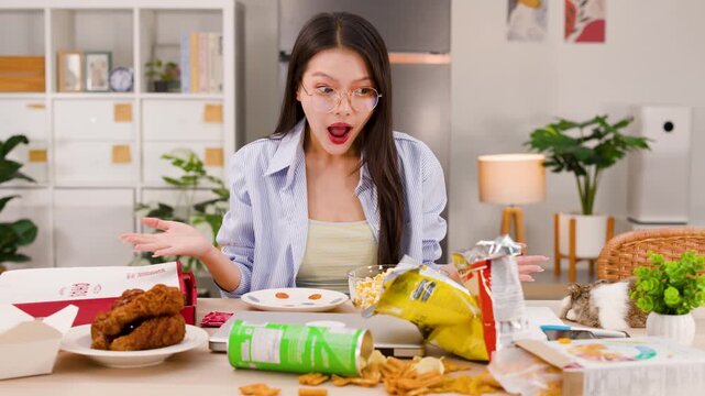 Shocked Asian Woman Sitting Before Table Mess of Junk Food