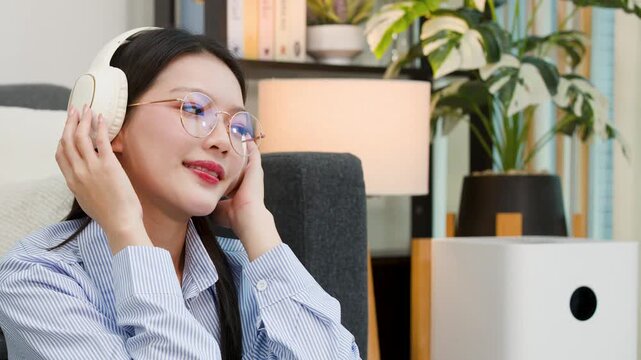 Asian Woman Wearing Headphones Listening to Music and Relaxing at Home