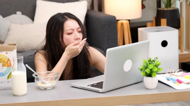 Tired Asian Woman Yawning While Working on Laptop at Home
