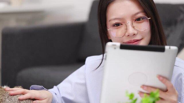 Young Asian Woman in Eyeglasses Browsing Digital Tablet on Living Room Sofa