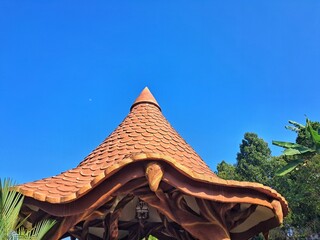 Terracotta fish scale roof tiles on conical pavilion spire against vibrant blue sky. © Fiqih