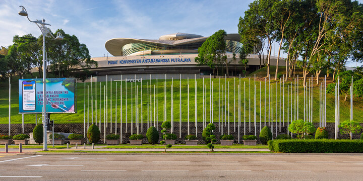 Putrajaya, Malaysia - February 20, 2025: Exterior view of the Putrajaya International Convention Centre with its distinctive roof, sloping green lawn, and numerous flagpoles under a blue sky