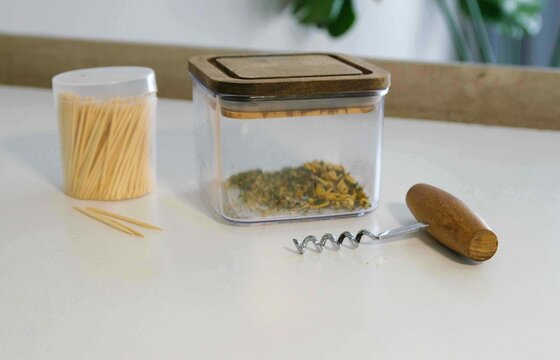 Container with herbs, toothpicks, and corkscrew on a white table in a kitchen setting