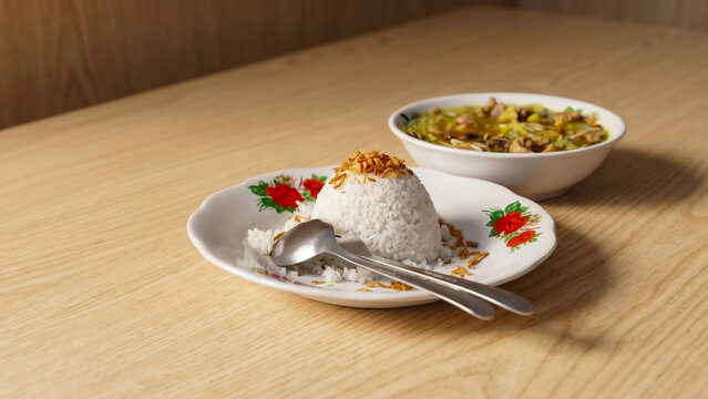 Delicious homemade soto ayam served with rice and fried shallots on classic ceramic tableware, illuminated by warm lighting with abundant copy space on the left.