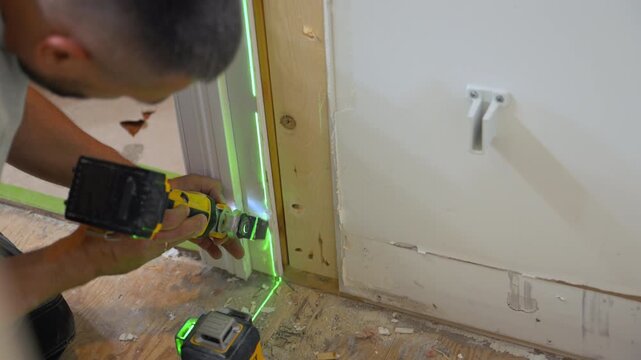 Carpenter using an oscillating power tool to cut drywall and wood around a frame during home renovation.