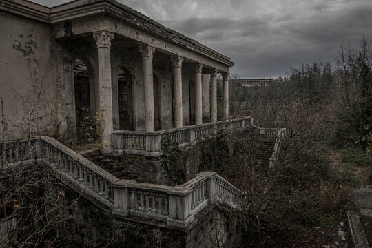 Ruins of Sanatorium Medea in Tskaltubo, Georgia, with elegant classical columns emerging from decay beneath a dark, gloomy atmosphere.
