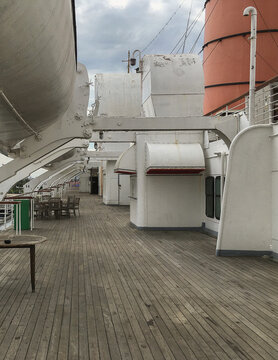 Deck chairs and wood teak outdoor promenade boat deck on luxury oceanliner, cruiseship or cruise ship liner Mary on sunny day with signs of decay