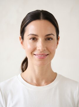 Smiling woman facing camera in studio headshot. Natural beauty and skincare portrait. Friendly professional profile for wellness and personal care. Clean background with copy space.