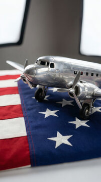 studio shot of a classic silver retro toy airplane resting on a flat, neatly pressed American national flag. The vintage twin-engine model features metallic aluminum finishes, tiny spinning 