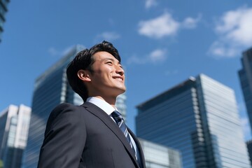 Fototapeta premium 青空広がる都会で未来を見上げる笑顔の若いビジネスマン