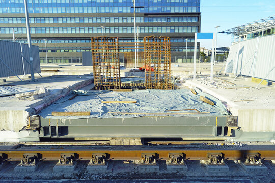 Rebar column cages rise from platform foundation beside tracks. Highlights reinforced deck fabrication, vertical support preparation, and rail station rebuilding alongside live operational railway.