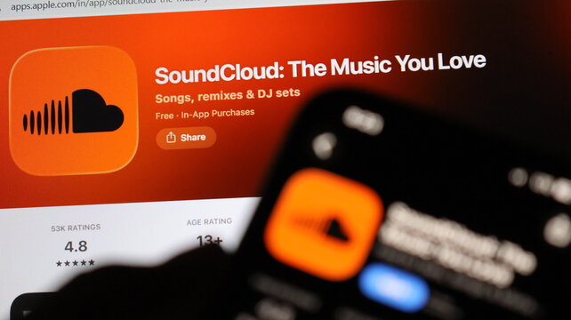 Smart phone presenting SoundCloud music application interface over computer screen featuring official platform banner.
