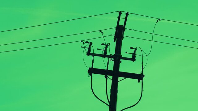 Silhouette of utility pole with power lines and transformer hardware against a green sky background