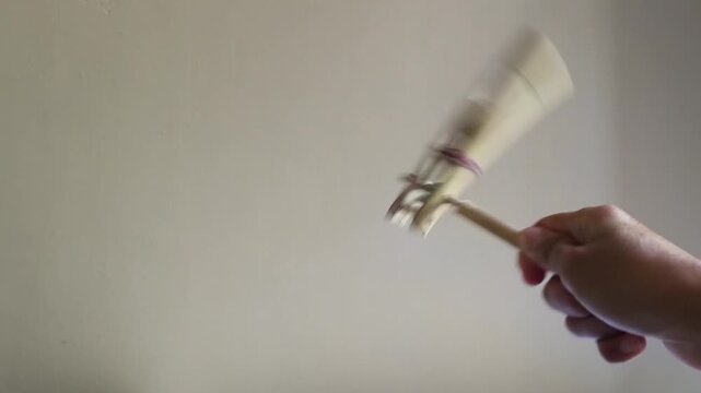 Person playing traditional Indonesian bamboo noisy toy spinning hand craft against plain wall