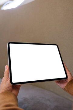 Vertical mockup image of a woman holding digital tablet with blank white desktop screen in cafe