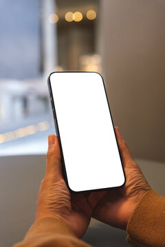 Vertical mockup image of a woman holding and using mobile phone with blank desktop white screen at home