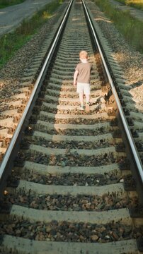 Small child steadily moves away on parallel train rails under warm light. scene emphasizes path ahead and surrounding gravel grass with no other people or vehicles