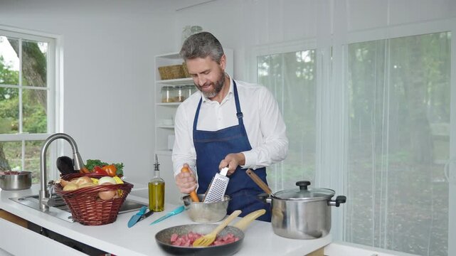 A man chops ingredients for homemade meal in kitchen. A chef preparing a vegetarian dish in the kitchen. A cook with raw vegetables. A man in an apron chops vegetables for a nutritious lunch at home.