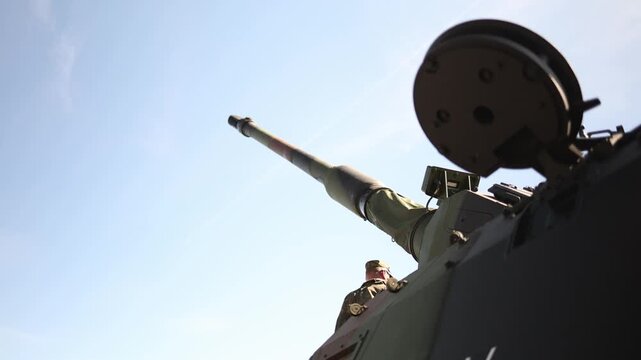 Low angle closeup of armored tank turret and long main gun barrel reaching into clear blue sky showing heavy military firepower and modern battlefield engineering outdoor
