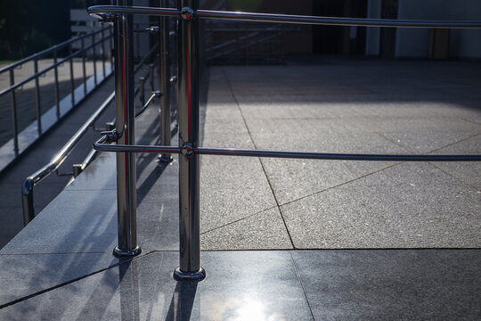 Stainless steel handrails and safety barriers installed on granite tile terrace near building entrance ramp