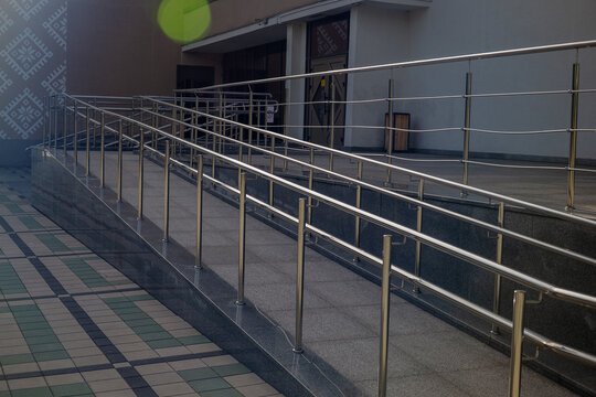 Accessible building entrance ramp made of stone tile with shiny stainless steel handrails for wheelchair users