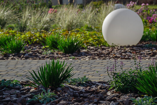 Large white round lamp standing on bark mulch bed in beautifully landscaped public park garden with tiled pathway and copy space