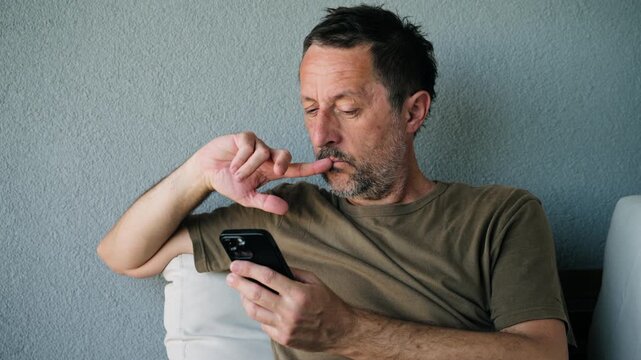 Serious, middle-aged man stares at his smartphone with a pensive expression. The image conveys concentration, concern, and everyday mobile communication in a neutral setting. 4K.