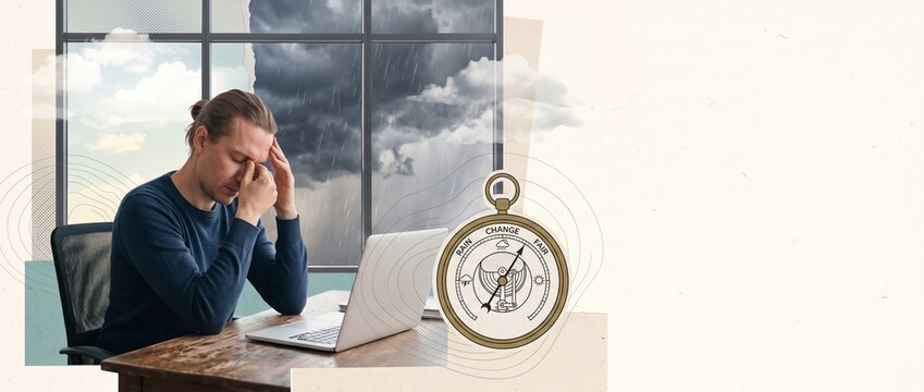 Weather-sensitive man with headache working on laptop during stormy weather, illustrating meteosensitivity, barometric pressure changes, fatigue and reduced wellbeing