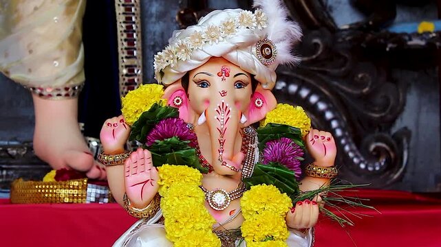 Mangalmurti Ganesh idol closeup wears floral turban, blesses devotees with raised hand, marigold and purple flower garlands, Ganesh Chaturthi India.