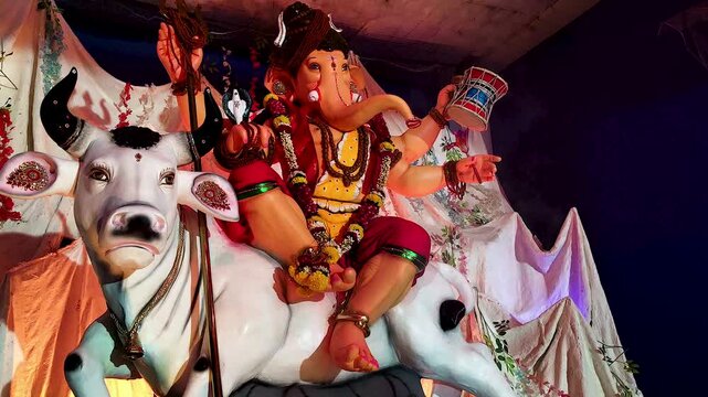 Ganesha idol dressed as Shiva sitting on Nandi bull with trishul and damru, snowy mountain decoration in Ganpati pandal India, colorful festival lighting.