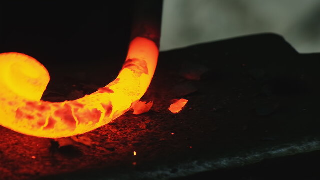Seasoned smith repeatedly applies pressure to softened iron with hammer. Skilled craftsman processes incandescent steel in workshop