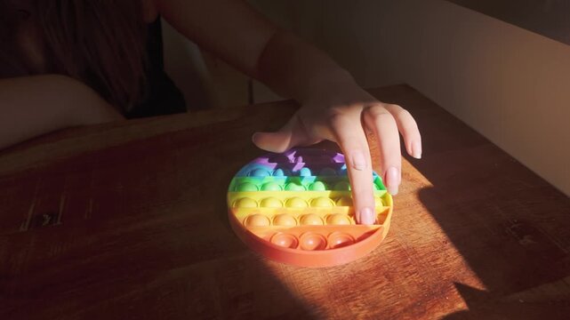 Close up of hands playing with colourful Pop-It and squishy ball toys in a low lit room, illustrating tactile sensory play and relaxing leisure activity.
