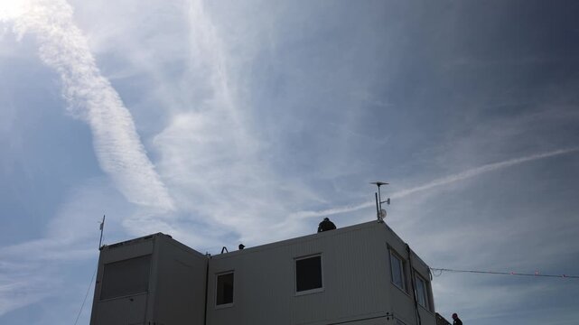 Security guard watches from the roof of a temporary building while monitoring the surrounding area from an elevated position under a wide cloudy daytime sky during patrol