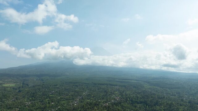 Clouds drift over lush green foothills and distant slopes of Semeru volcano in daylight