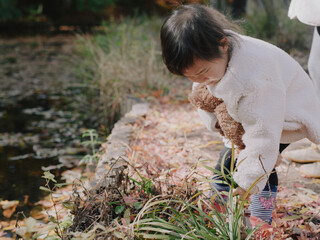 Toddler in a white fleece leaning at the edge of an autumn pond © visualstory