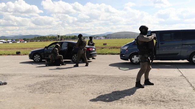 Police tactical team restrains suspect beside stopped vehicles during training while armed officers secure the area with protective gear shields and coordinated responses
