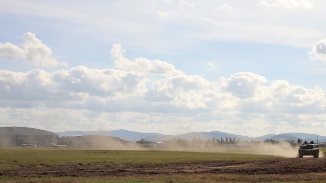Leopard 2A4 main battle tank drives across rough training ground raising a large dust trail during military demonstration showing armored mobility and tracked performance