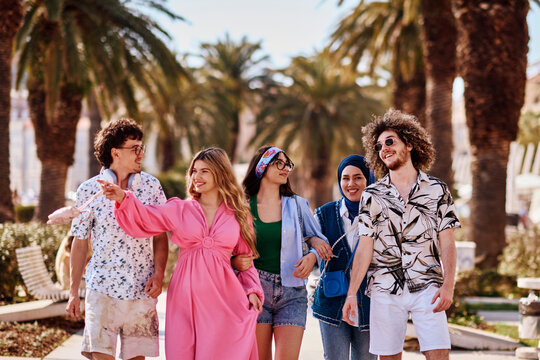 Diverse Group Of Friends Walking And Laughing Together On A Sunny Palm-Tree Lined Street
