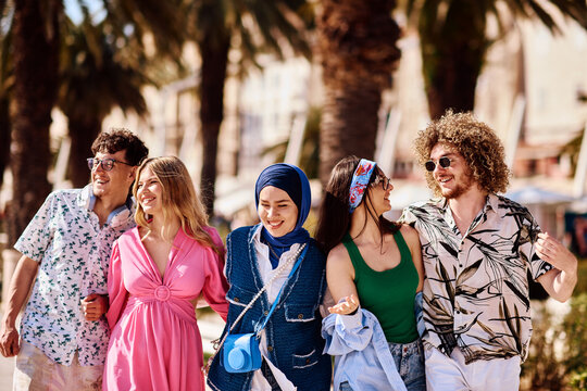 Diverse Group Of Friends Walking Together On A Sunny Coastal Promenade With Palm Trees