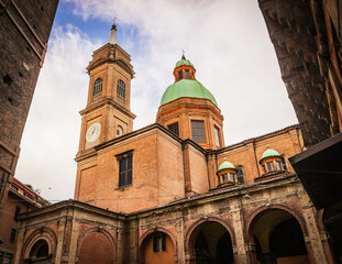 Low-angle view of the historic Santi Bartolomeo e Gaetano Church in Bologna, featuring its brick architecture, bell tower, arcades and green copper dome. © geografika