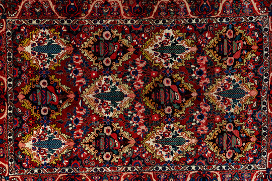 Persian and Central Asia wall carpet with abstract oriental pattern. Ornate red rug with symmetrical floral motifs, intricate geometric borders, and richly patterned woven textile surface