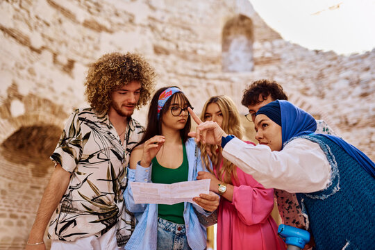 Diverse Group Of Young Tourists With Map And Local Guide Exploring Historic Ruins Together