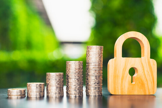 Financial security and money protection concept, wooden padlock standing beside rising stacks of silver coins on table, representing capital safety, wealth safeguard, and banking deposit.